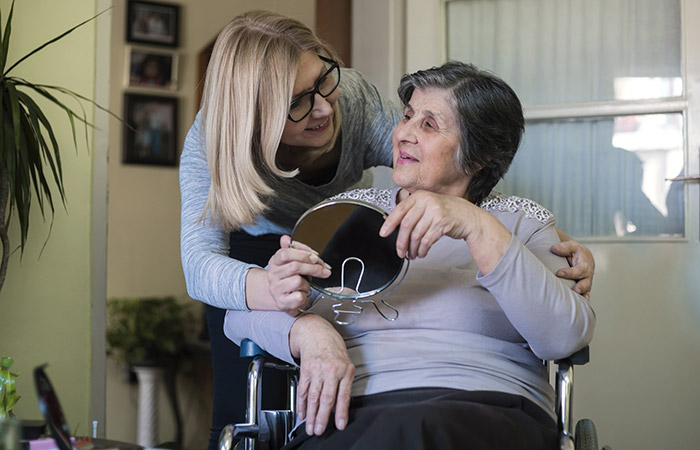 Une femme tenant un miroir pour une personne âgée en fauteuil roulant